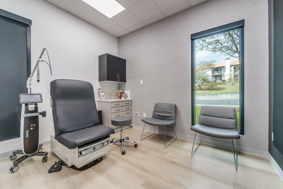 Treatment room with exam chair, laser device, seating, and large window