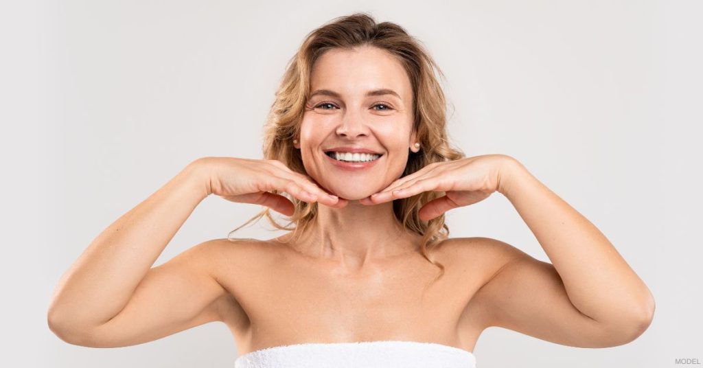 A woman with radiant skin holding their hands to their face. (Model)