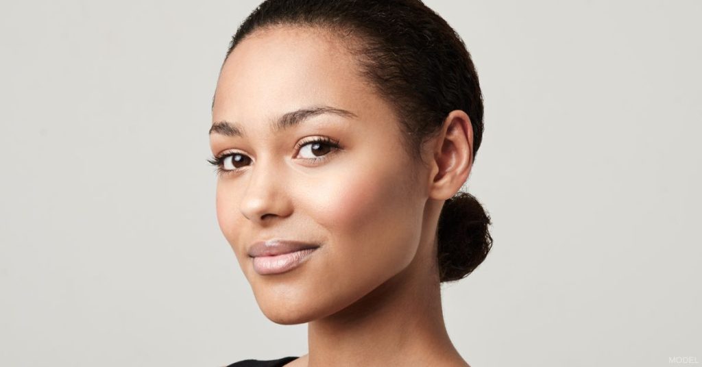 young woman (model) with smooth, clear skin on a light gray background