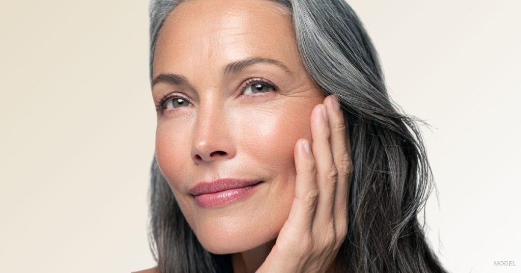 Mature woman smiling and holding her face. (Model)