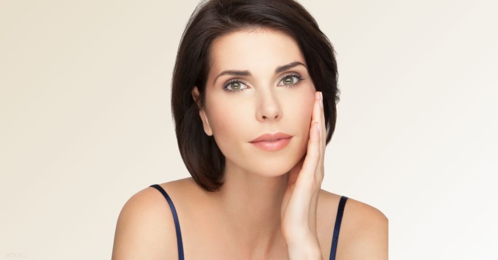 Woman touching her face after upper and lower blepharoplasty (model)